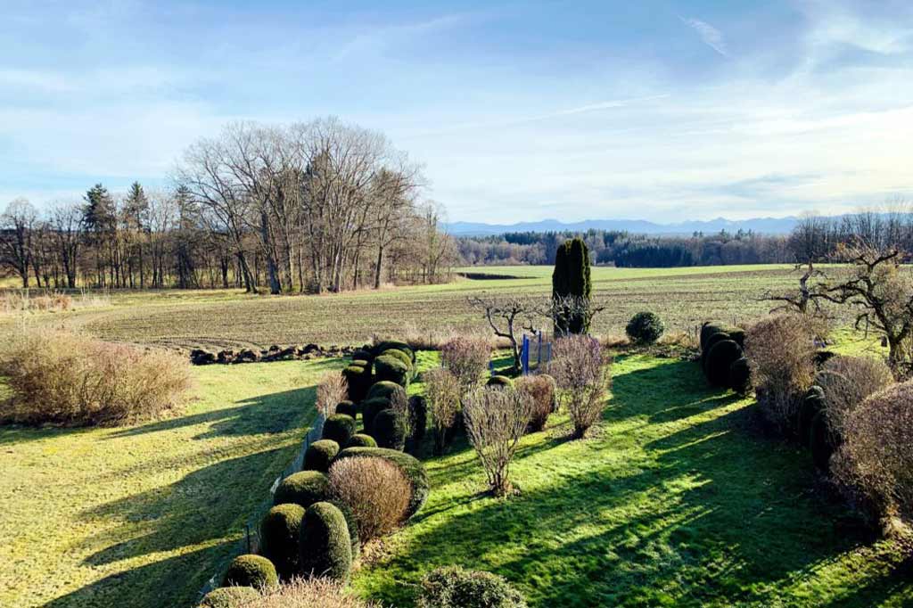 Ausblick vom Balkon in den großen, grünen Garten mit Bergen am Horizont